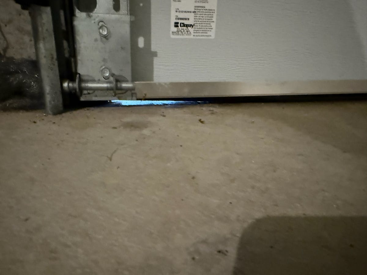 Read How to Rodent-Proof Your Residential Garage Door (Before Mice Move In) close-up of a garage door with daylight coming in from the bottom right corner providing space for pests to enter