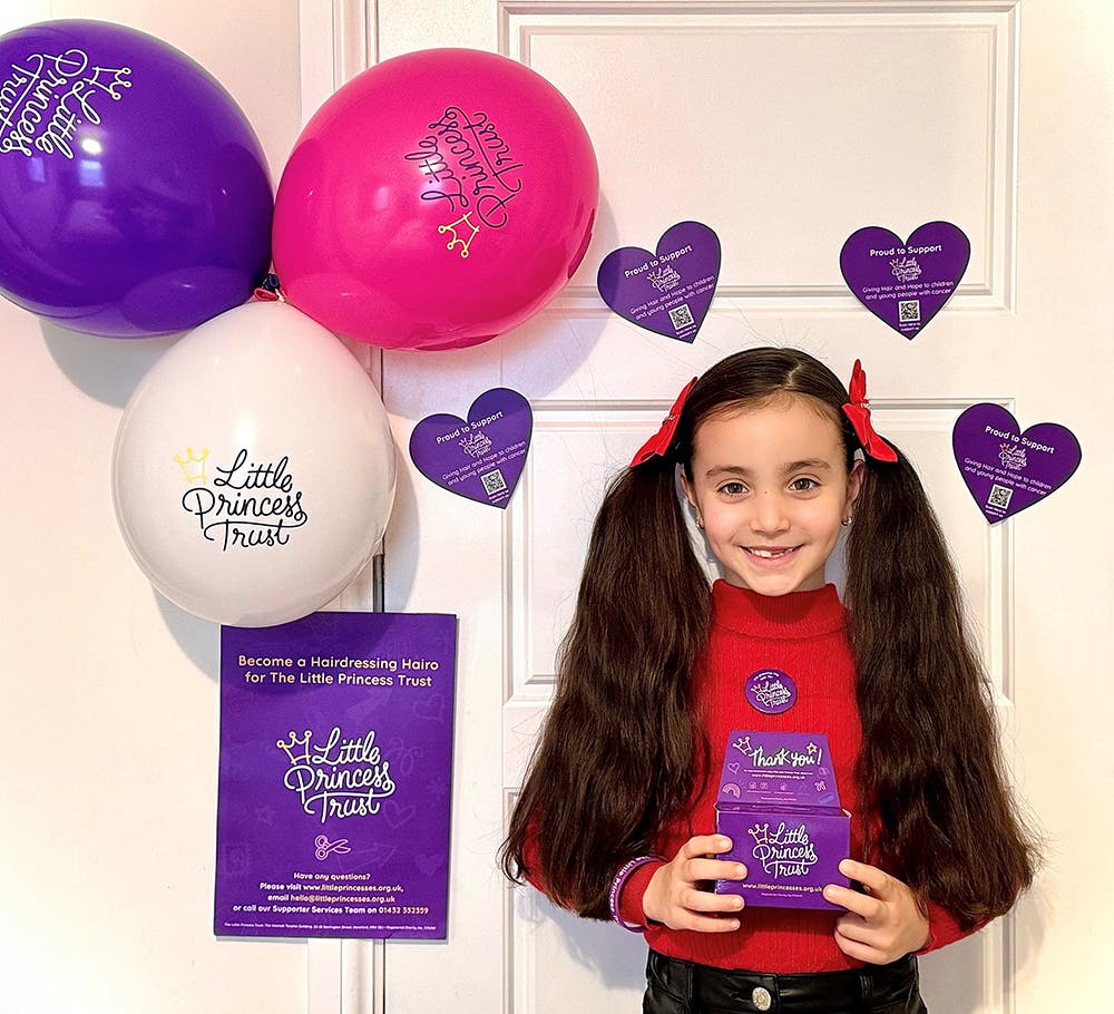 Delilah smiling with her fundraising materials and Little Princess Trust balloons.