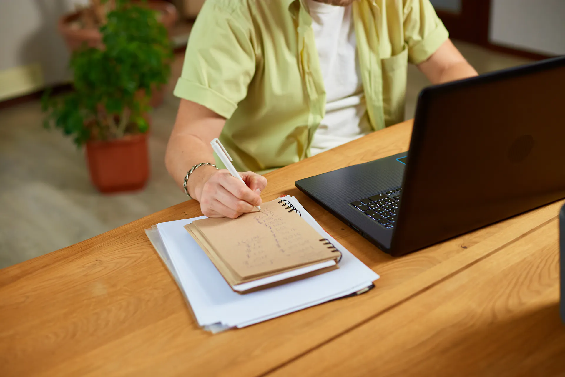 Pessoa faz anotações em um caderno ao lado de um notebook, representando planejamento de estratégias de marketing e organização do consultório.