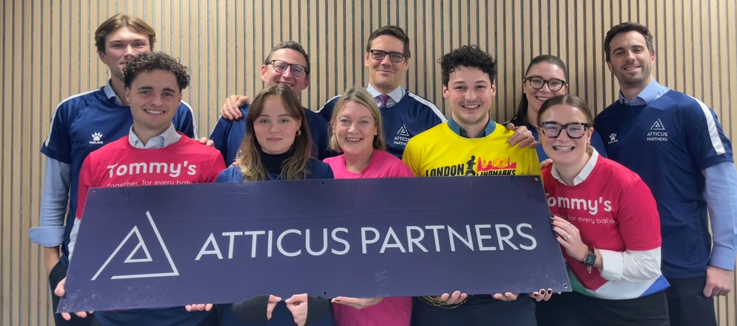 A group of runners smiling in Tommy's and London Landmarks branded tops holding an Atticus Partners sign