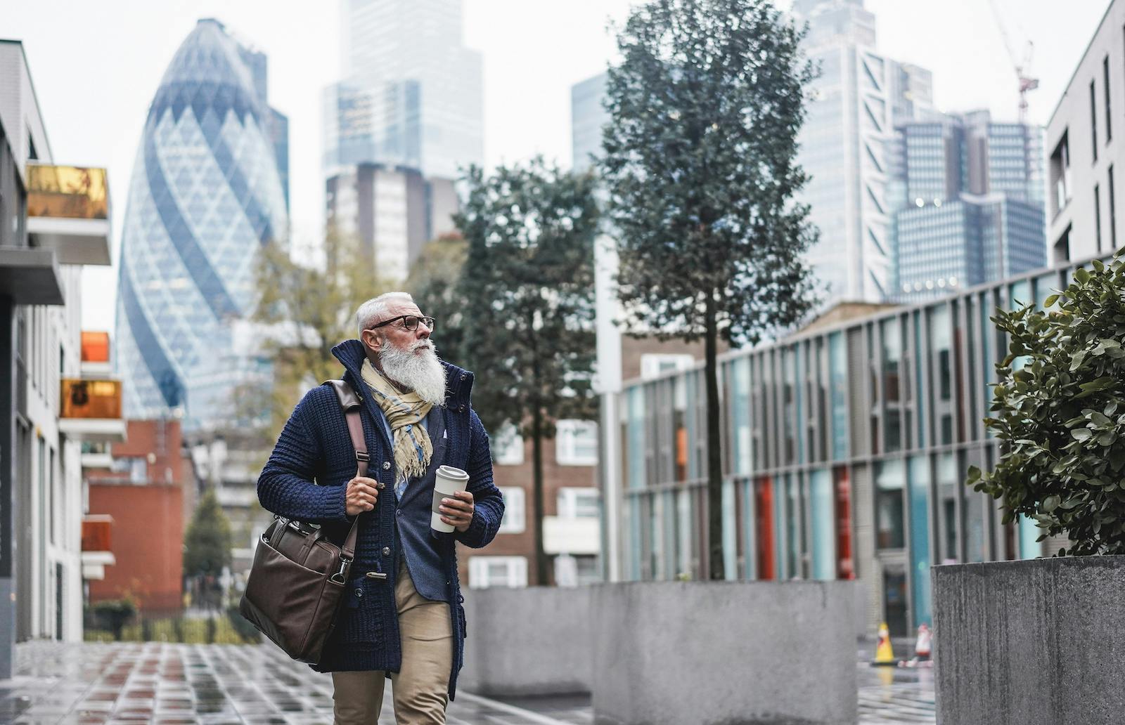 Bearded man carrying a coffee cup and shoulder bag on a walkway in London