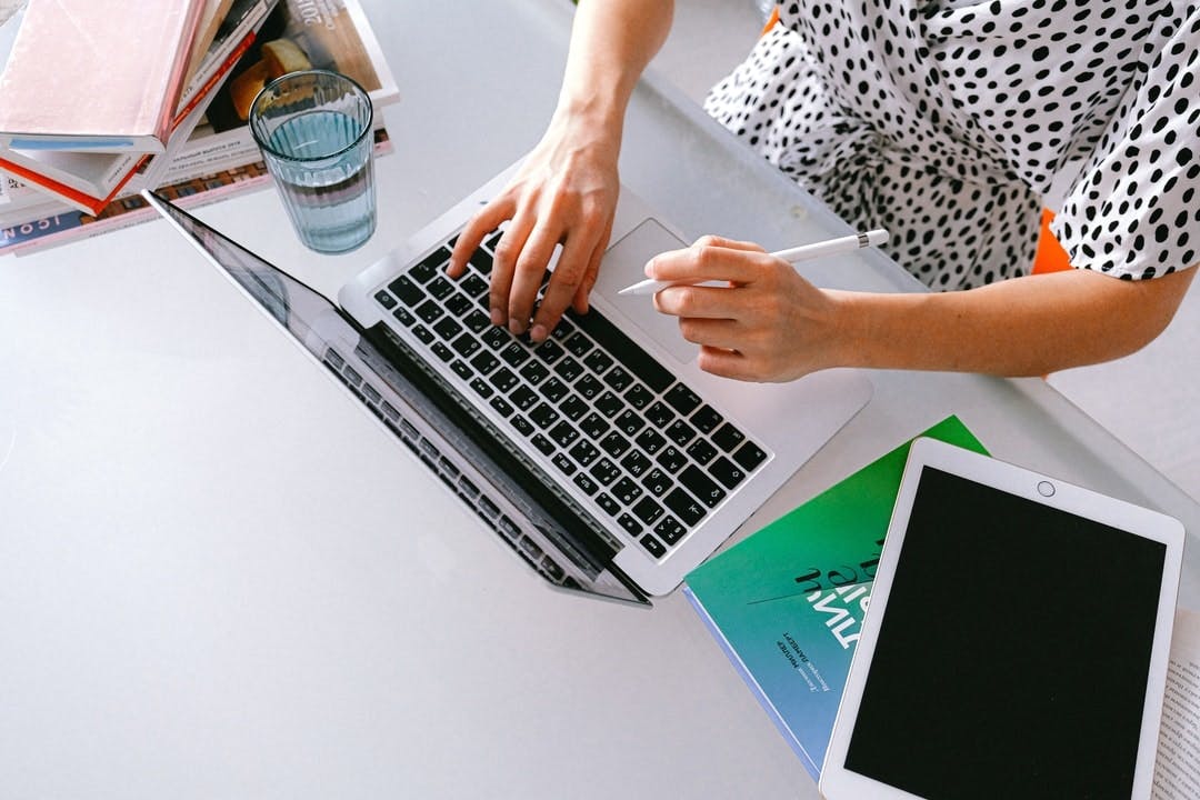 a female freelancer types on her laptop while holding a pen, seen from above