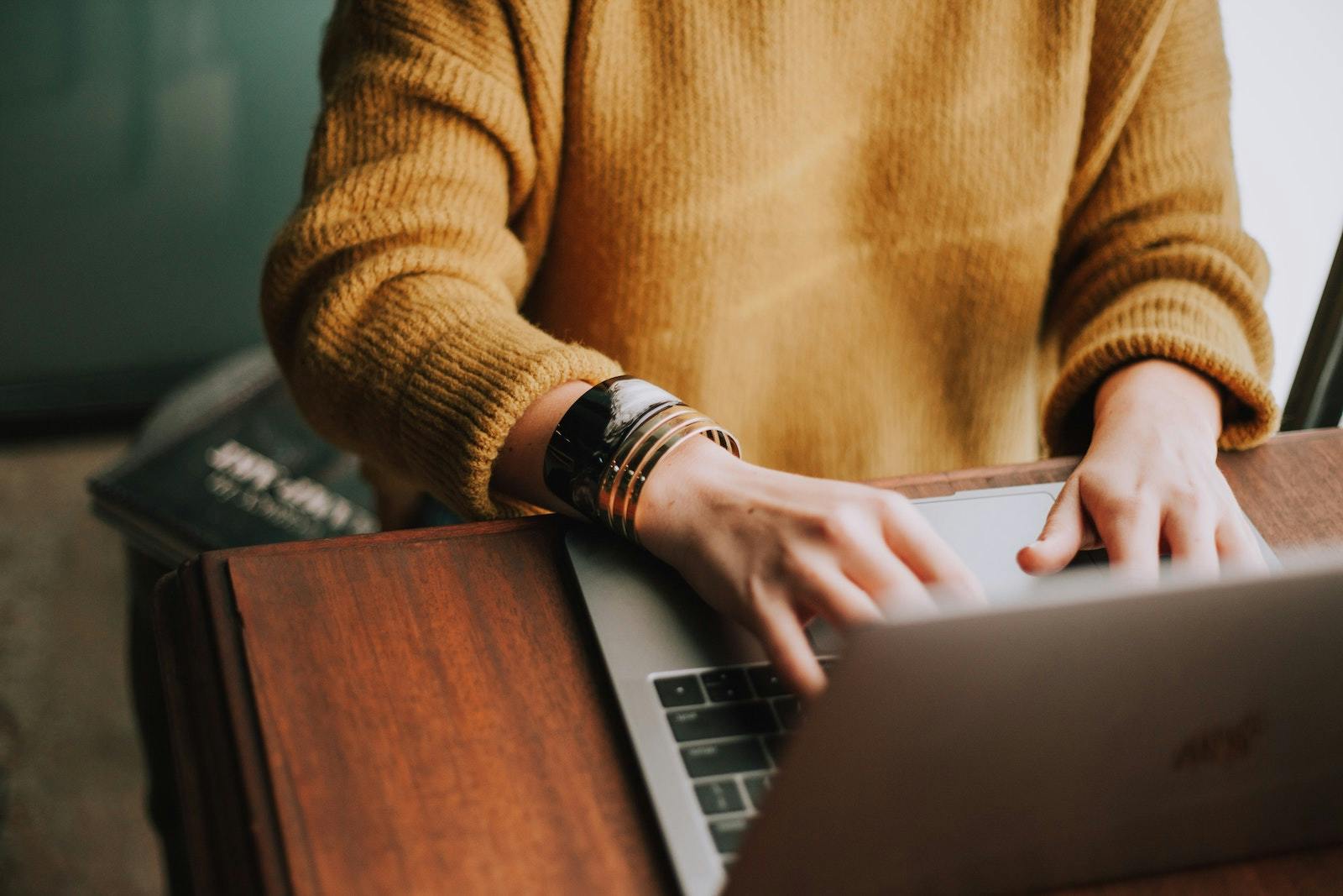 person in mustard yellow sweater typing on a laptop