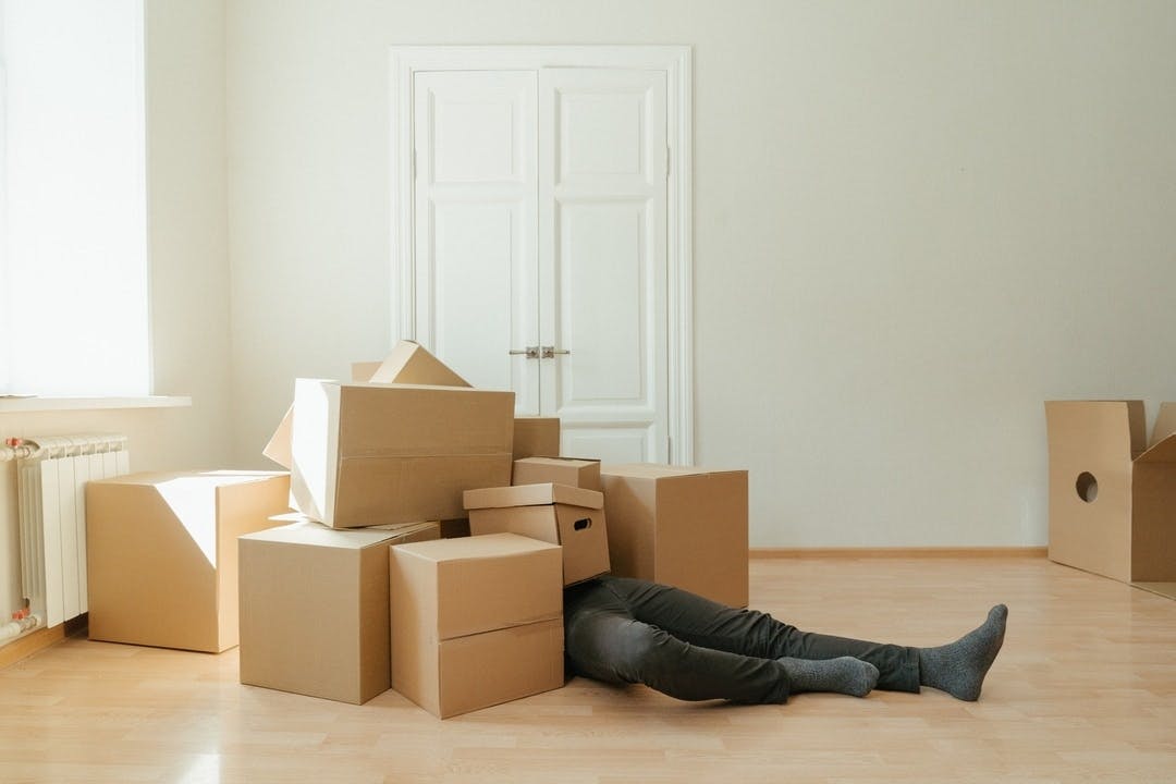 a person buried by a pile of moving boxes while relocating, only their legs can be seen sticking out of the pile