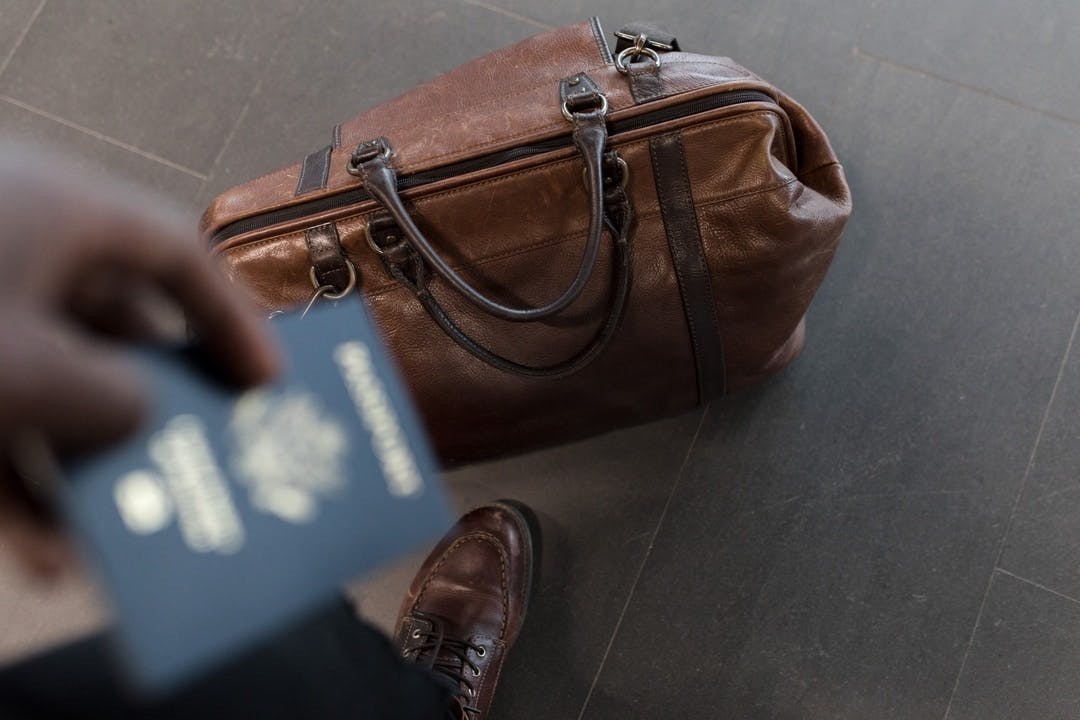 a relocating employee shaws the cover of his passport and suitcase while waiting at the airport