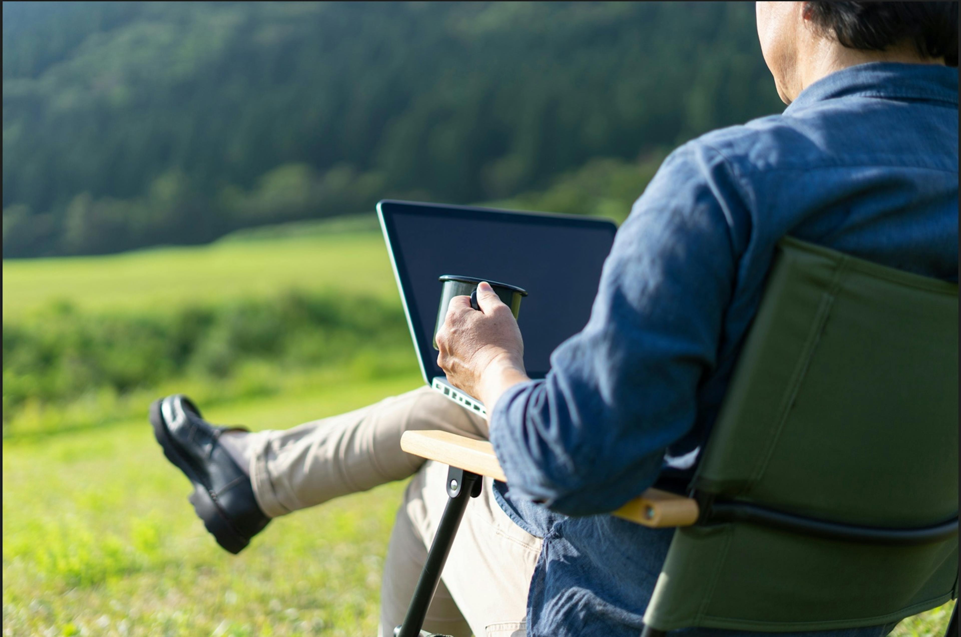 a middle aged man working from a laptop and camping chair in a meadow shows what global mobility can be