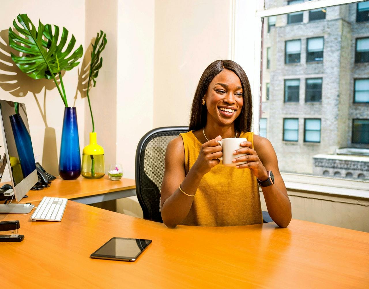 young woman sitting behind a desk, smiling while holding a coffee cup and creating a distributed framework for employees
