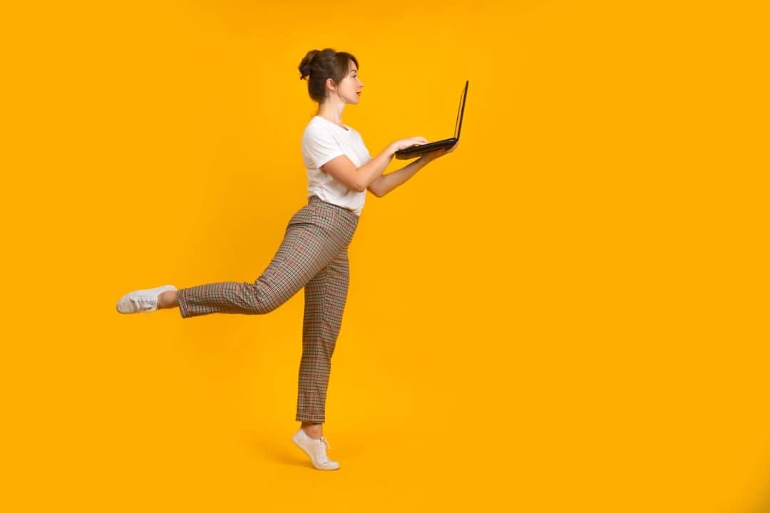 A female tech worker standing on tip-toe and holding her laptop while she works on recruiting international tech talent