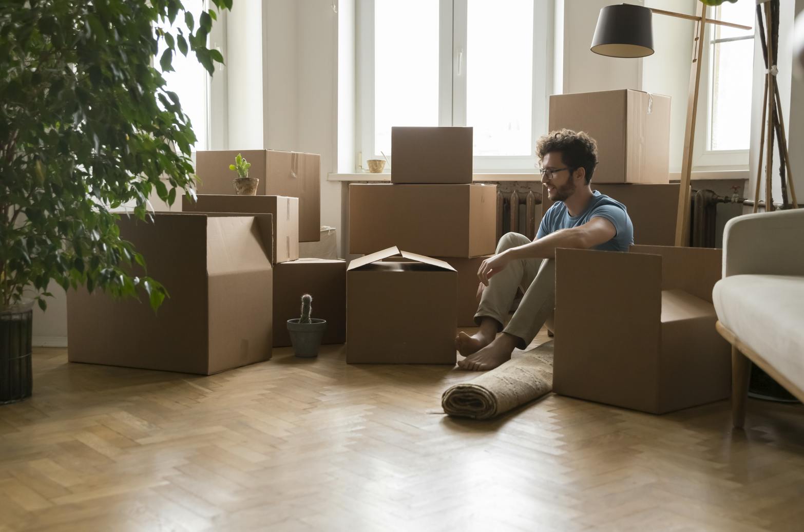 Man sits on the floor amid a pile of moving boxes after relocating