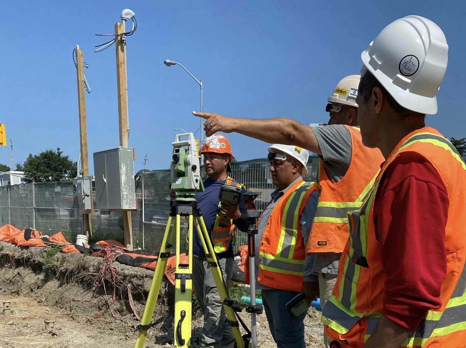 Construction workers in safety vests and helmets using surveying equipment at a construction site