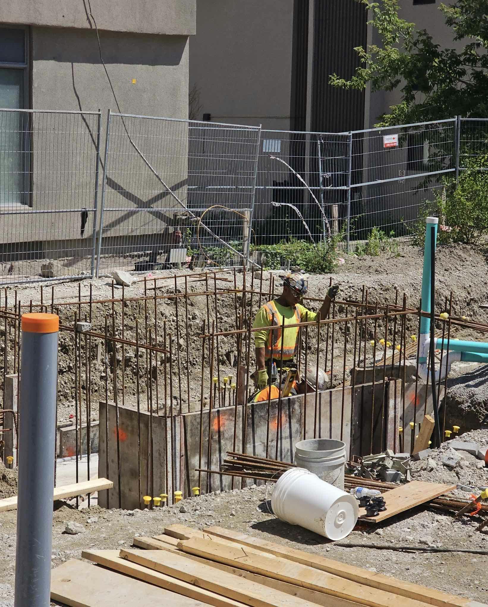 Construction worker standing in a rebar-reinforced excavation site at 215 Wellesley St., with fencing and building materials around