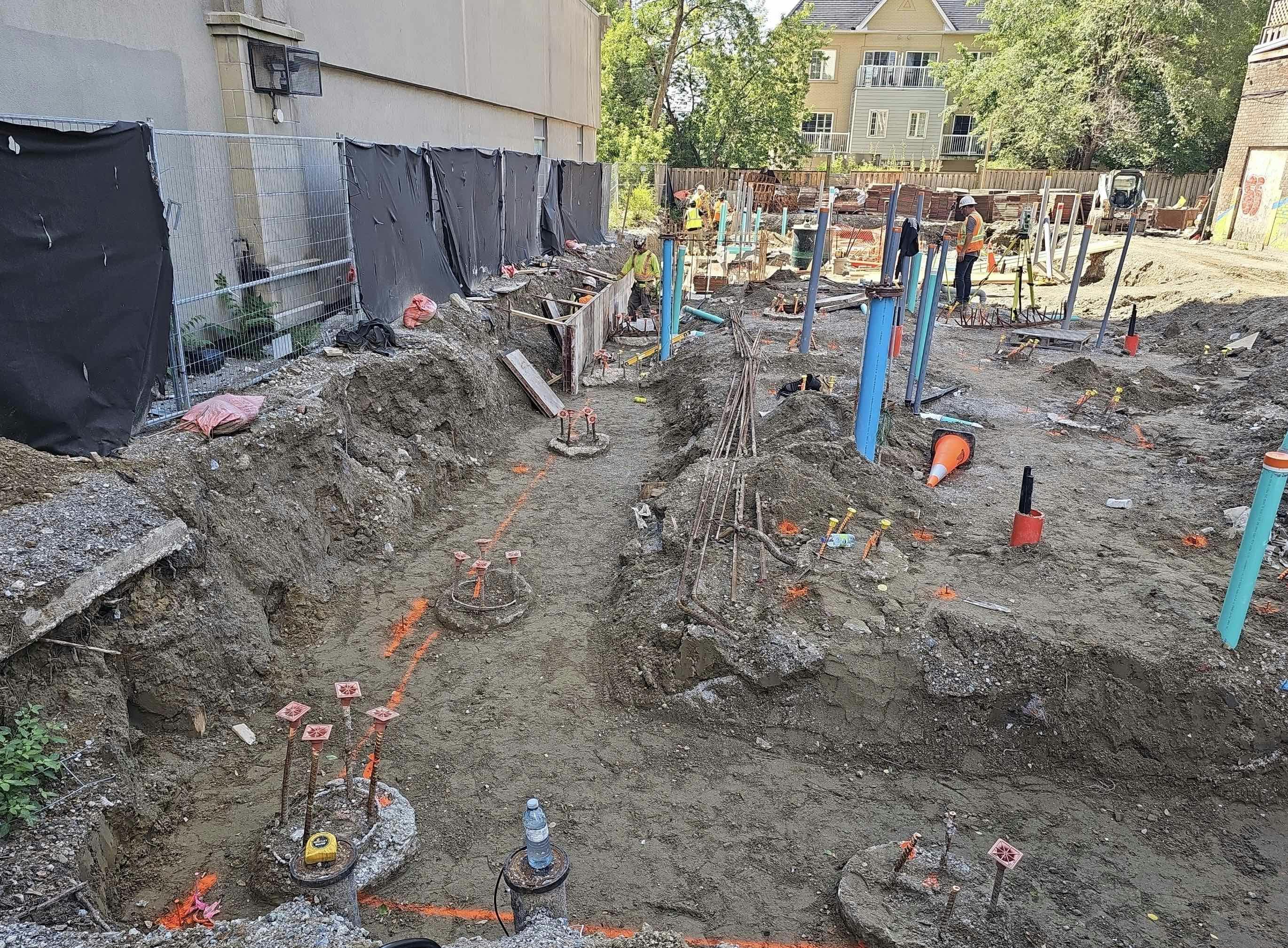 Excavation site at 215 Wellesley St. with exposed rebar, construction materials, and workers in the background