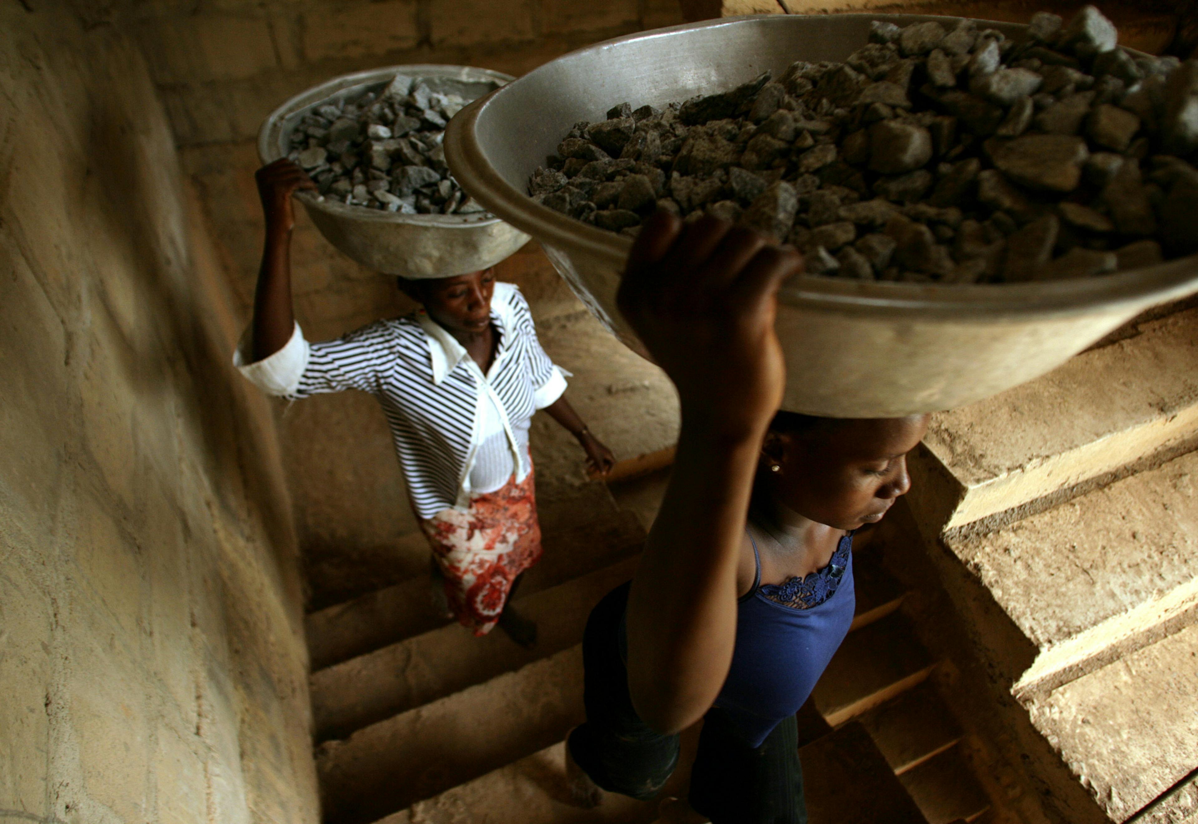 Two women carrying baskets with raw materials on their heads