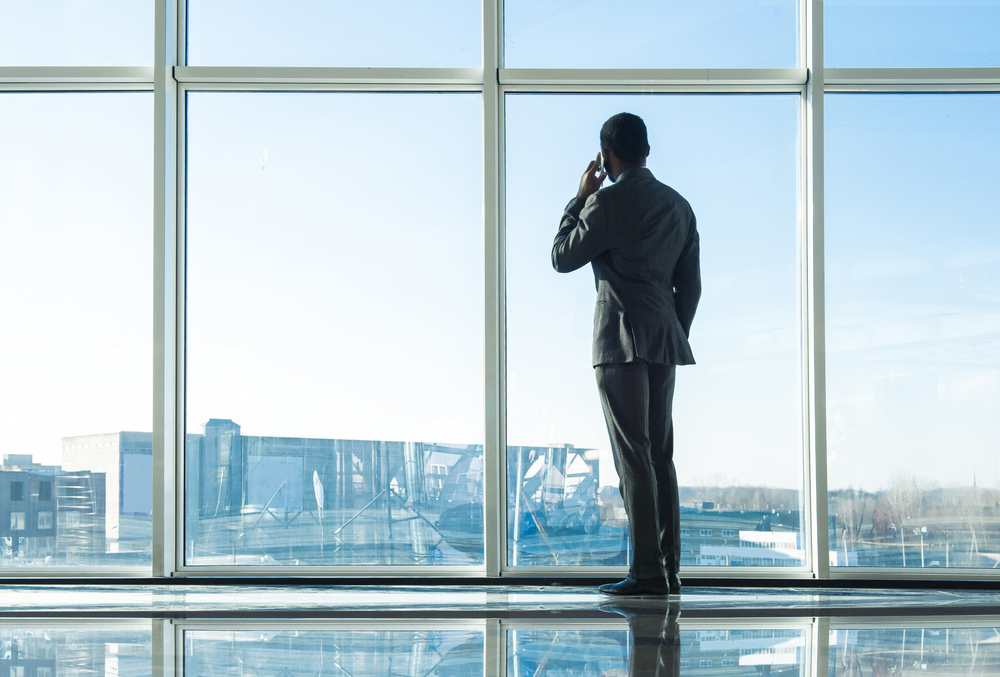 Maður í jakkafötum stendur við gólfsíða glugga og horfir út á meðan hann talar í farsíma