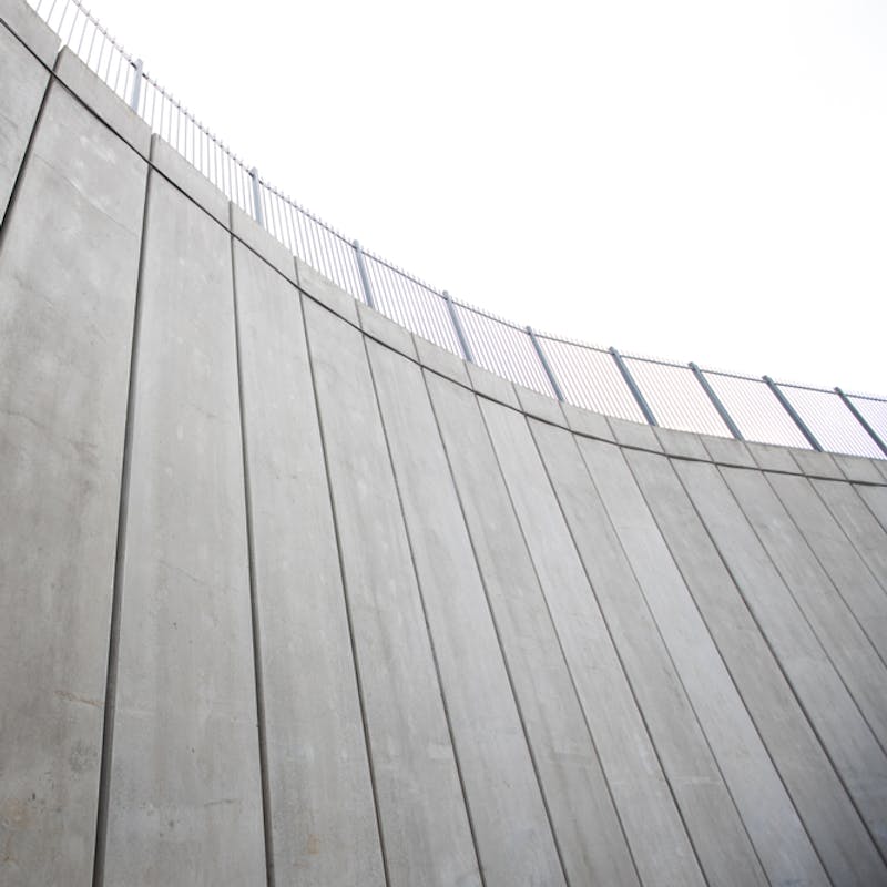 Horft upp eftir steyptum bogadregnum vegg, hvítur himinn