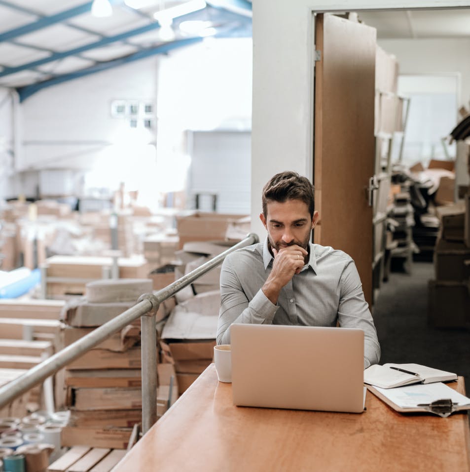 A logistics manager sits at his computer in the warehouse learning about the features of the new integrated delivery management system from Logtrade.