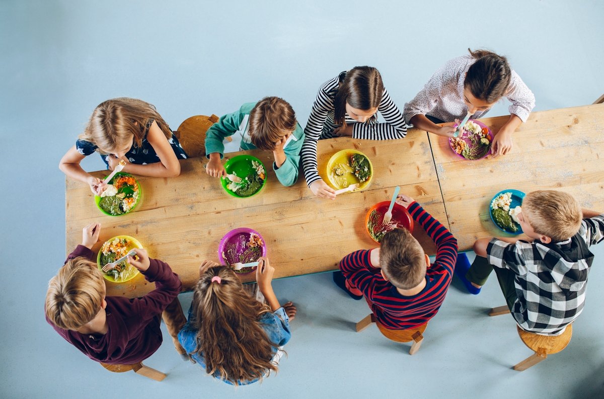 School children sitting at a long table eating food from colorful plates.