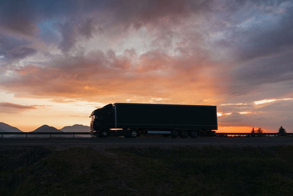 En transportör som är uppkopplad till Logtrades TA-system kör på en ökenväg med en solnedgång i bakgrunden.
