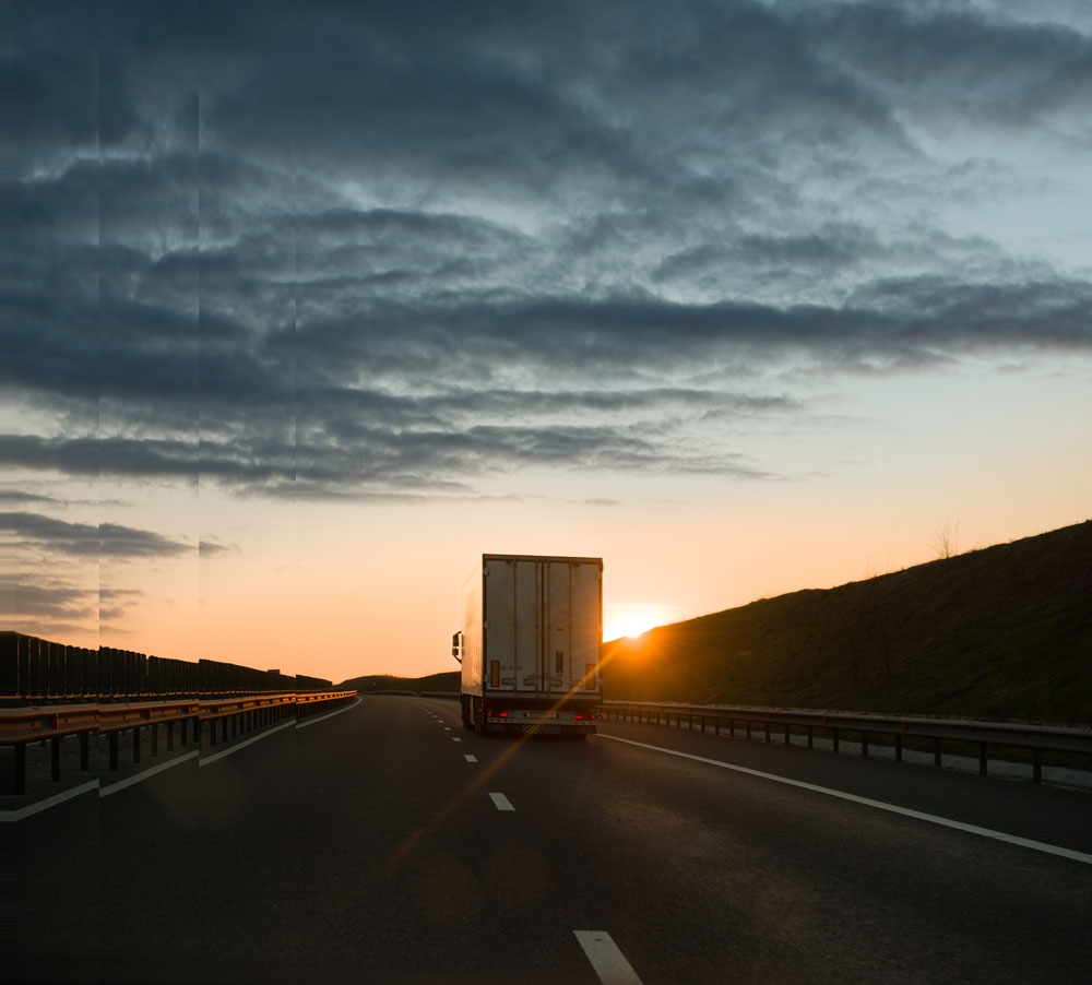 Bild av en ansluten lastbil som kör in i horisonten när solen går upp.