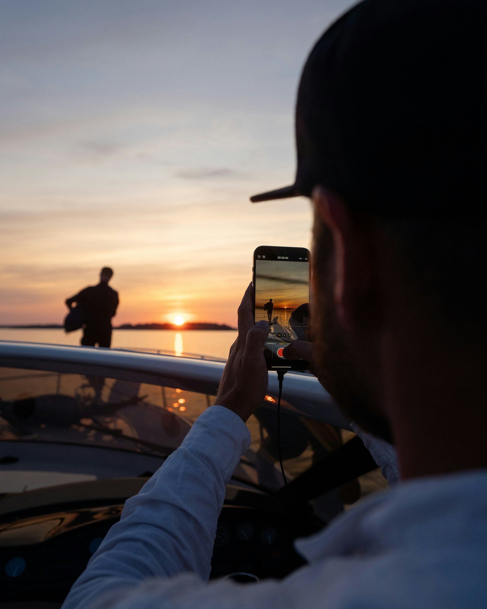 Man looking at a sunset through a phone camera on a boat
