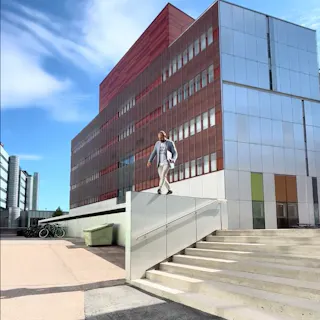 Tyylikkäästi pukeutunut mies kävelee kaidetta pitkin läppäri kädessään.