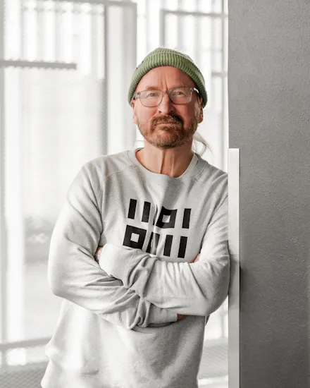 Pipopäinen mies nojaa seinään harmaa college päällään.