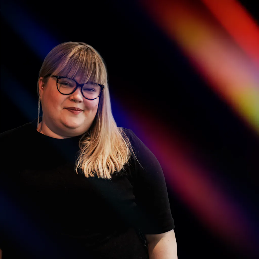 Nainen seisoo pimeässä värikkäiden valojuovien keskellä.