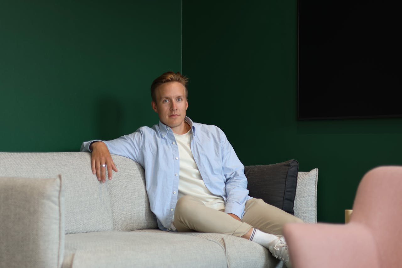 Man with a blue collar shirt sitting on a grey sofa.