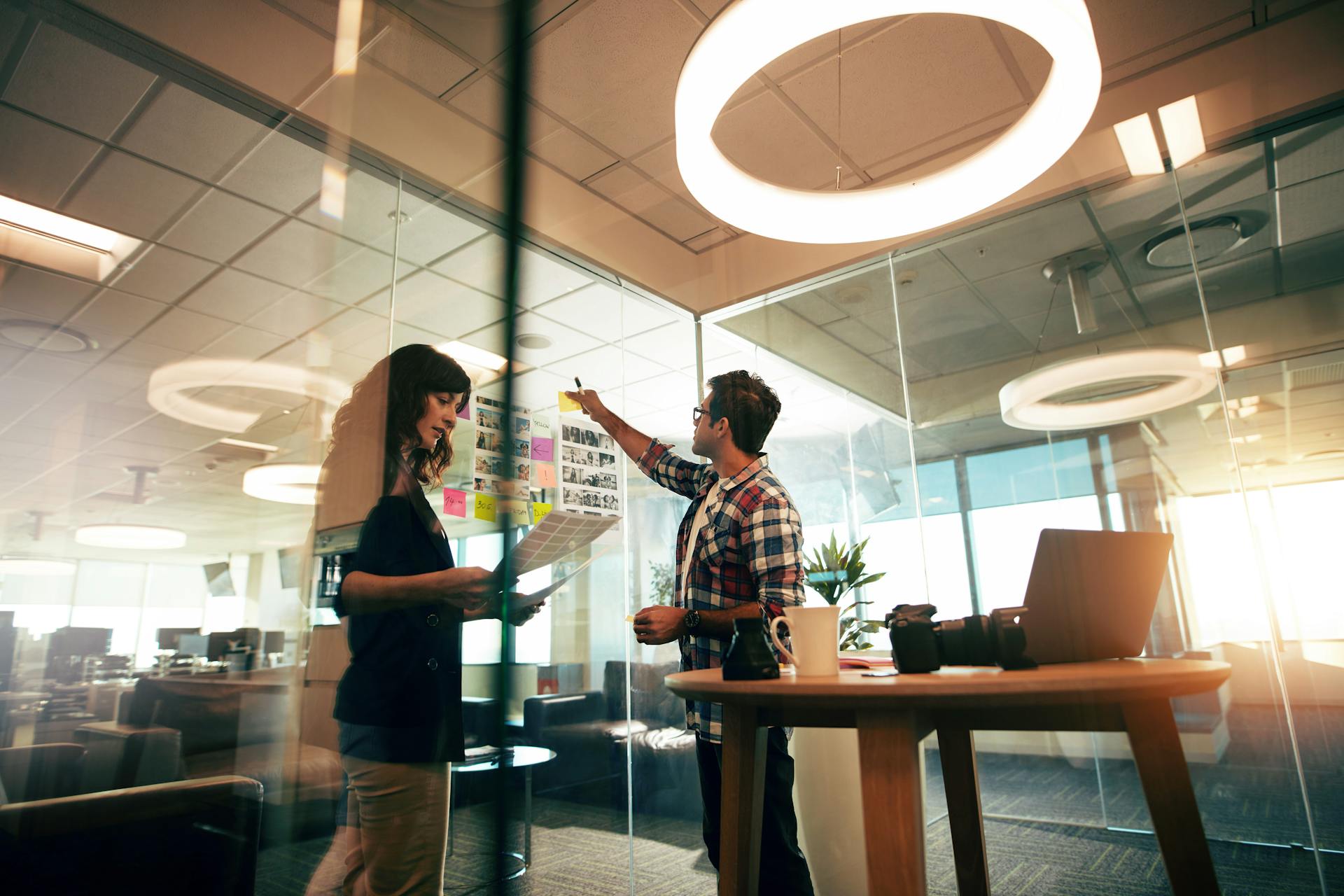 A woman and a man at an advertising agency, pointing a wall full of notes.