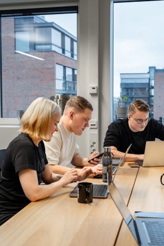 A girl and two boys on their laptops in front of a table.