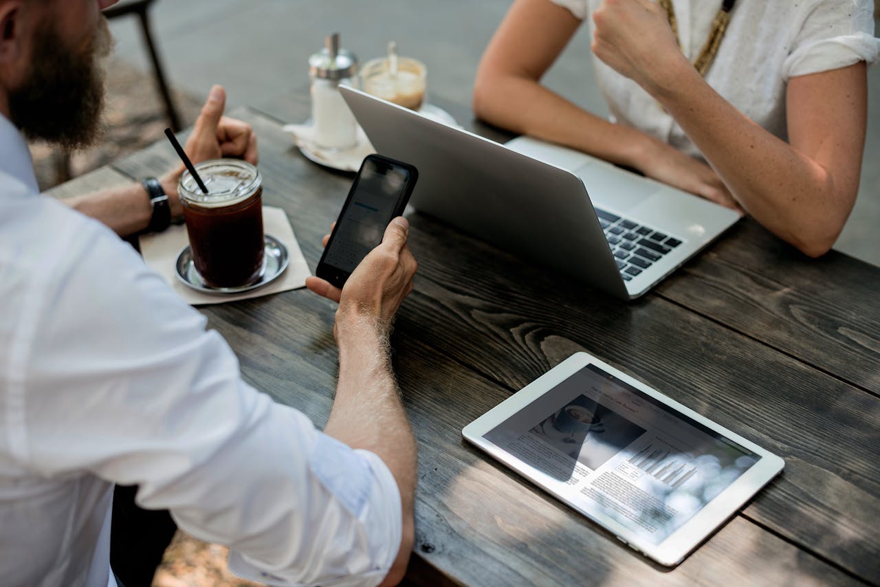 A man and a woman looking at a phone and a laptop on a coffee date.