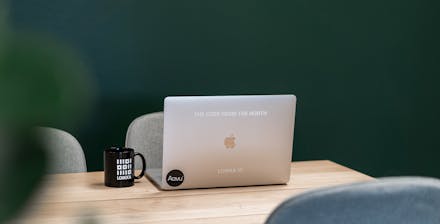 Kannettava tietokone vihreän seinän edessä, muki vieressä.