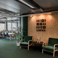Loikan logo komeilee lastulsevyä vasten heti toimistolle sisään tullessa. Ikkunoista sisään loistava valo luo vihreän lattiamaton kautta luonnollista tunnelmaa.