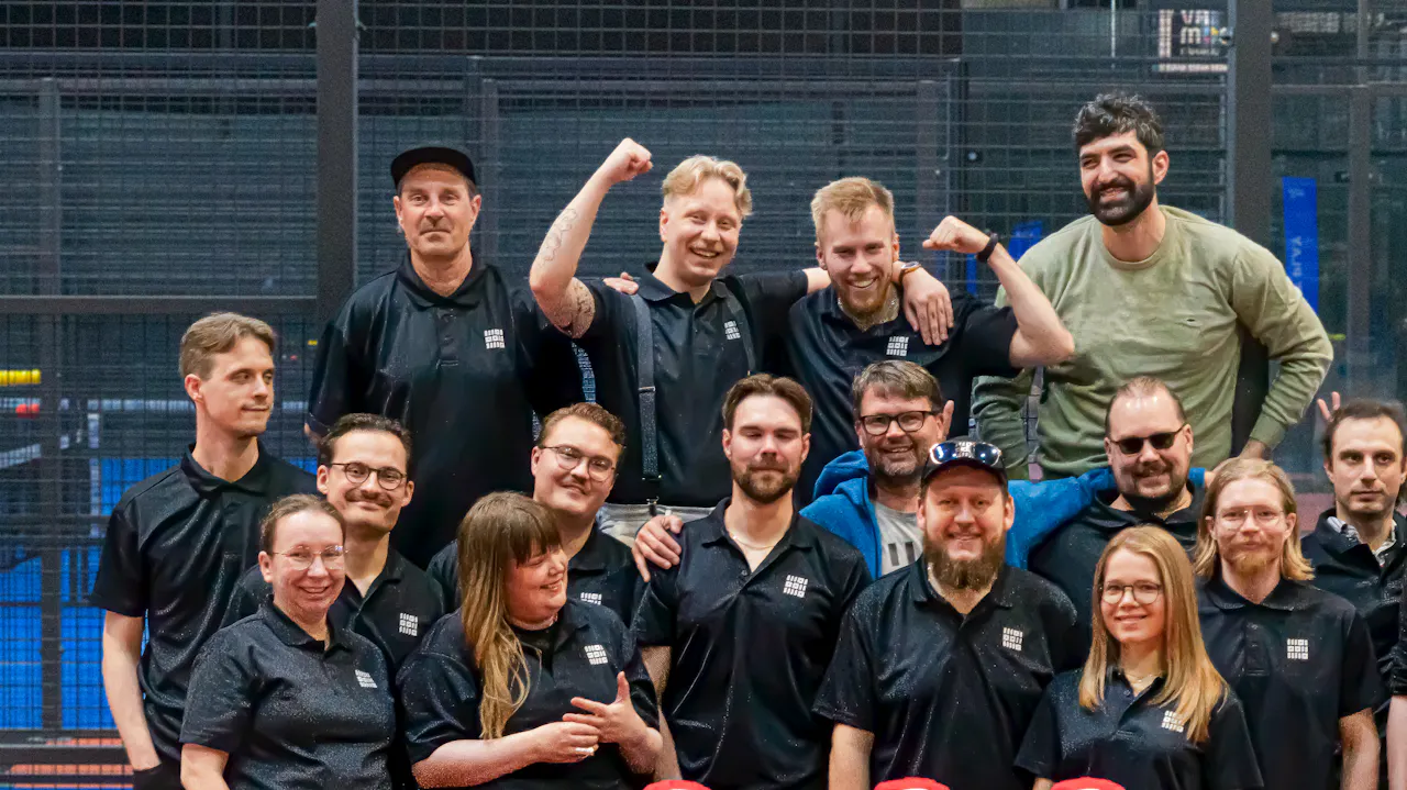 Loikan porukkaa poseeraa ryhmässä sinisten padelkenttien edessä.