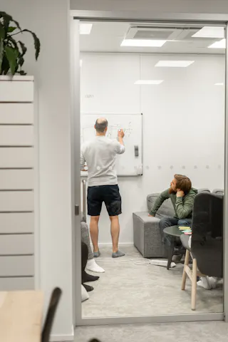 College-paitainen mies piirtää tussilla kaavioita valkotaululle.
