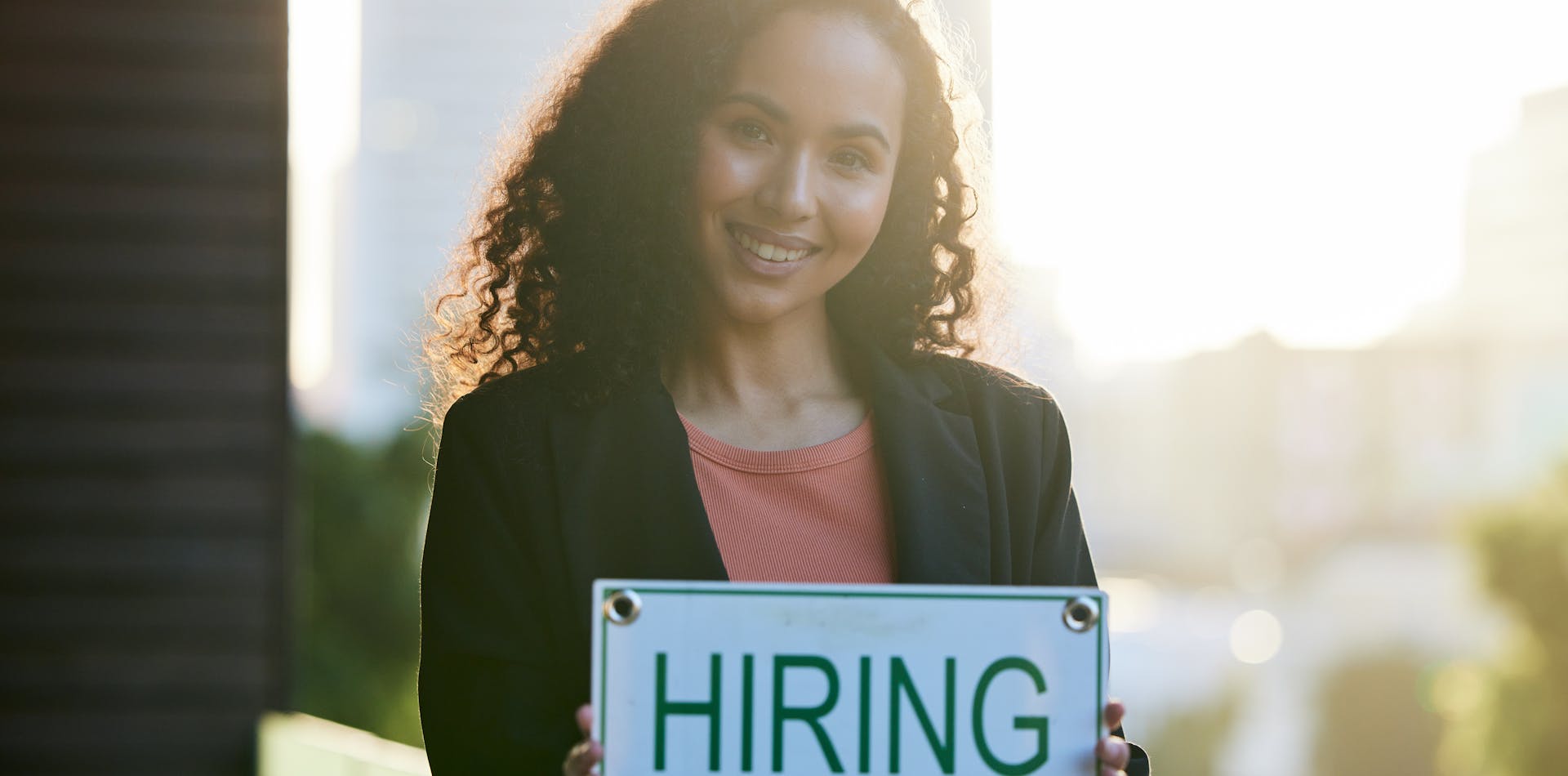 Woman surrounded by skyscrapers holding a hiring sign