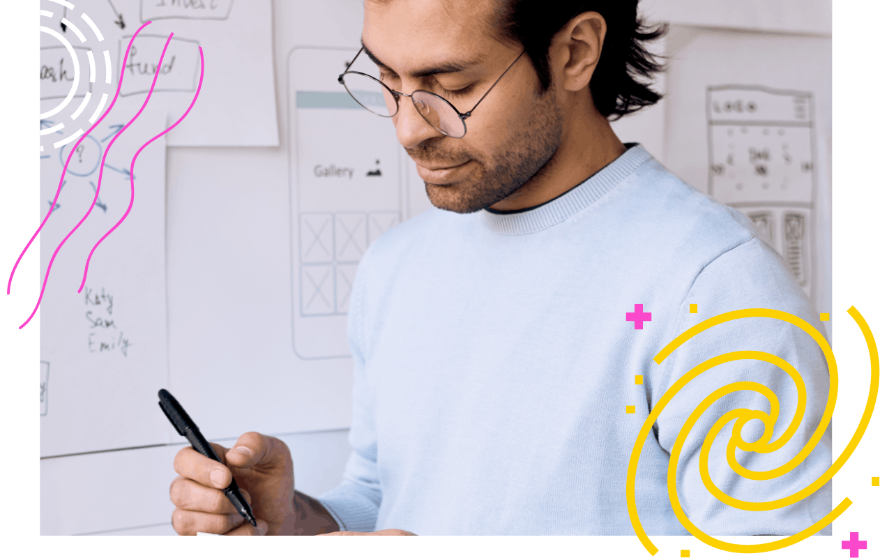 Man with glasses taking notes next to a whiteboard of mobile design mockups