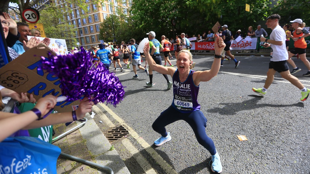 Meningitis Research Foundation marathoner flexing and smiling with celebrating onlookers. 