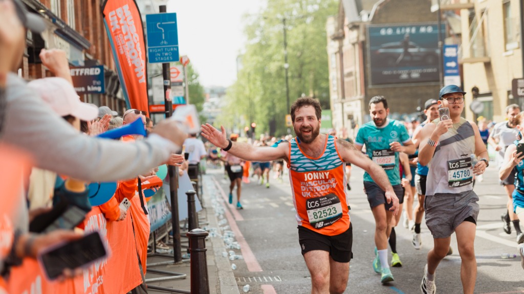 Muscular Dystrophy UK marathon runner smiling and giving high fives to cheering spectators.