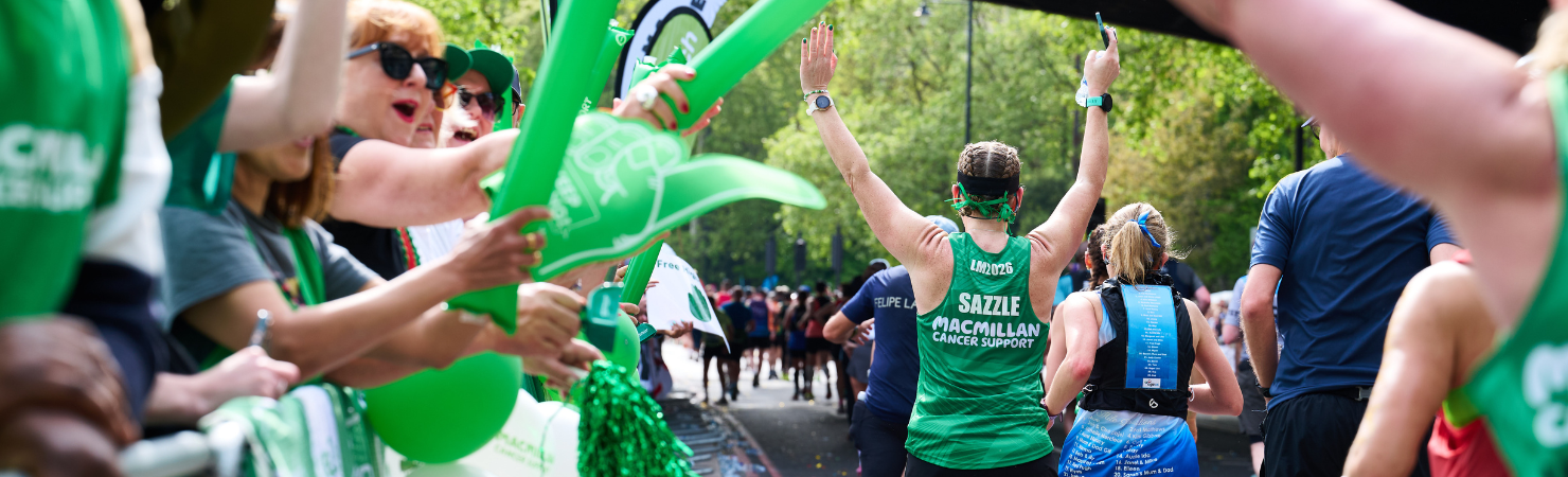 Macmillan Cancer Support runner raises both arms while passing cheering supporters at a road race.