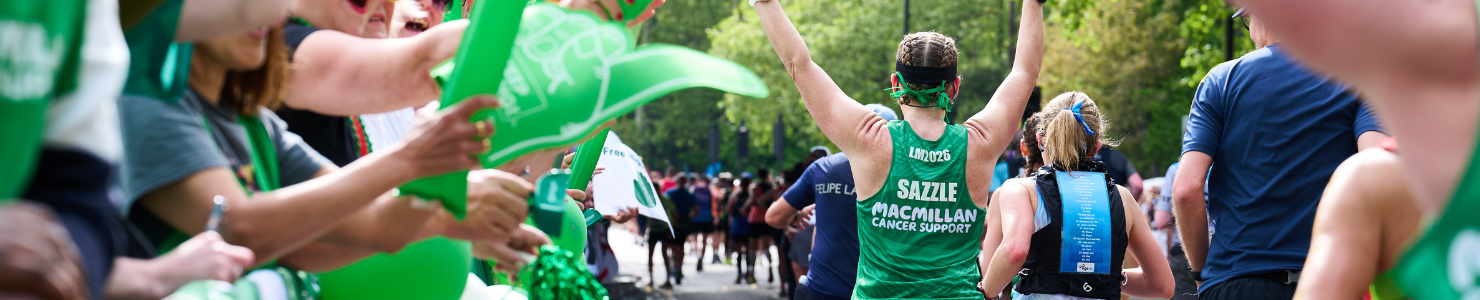 Macmillan Cancer Support runner raises both arms while passing cheering supporters at a road race.