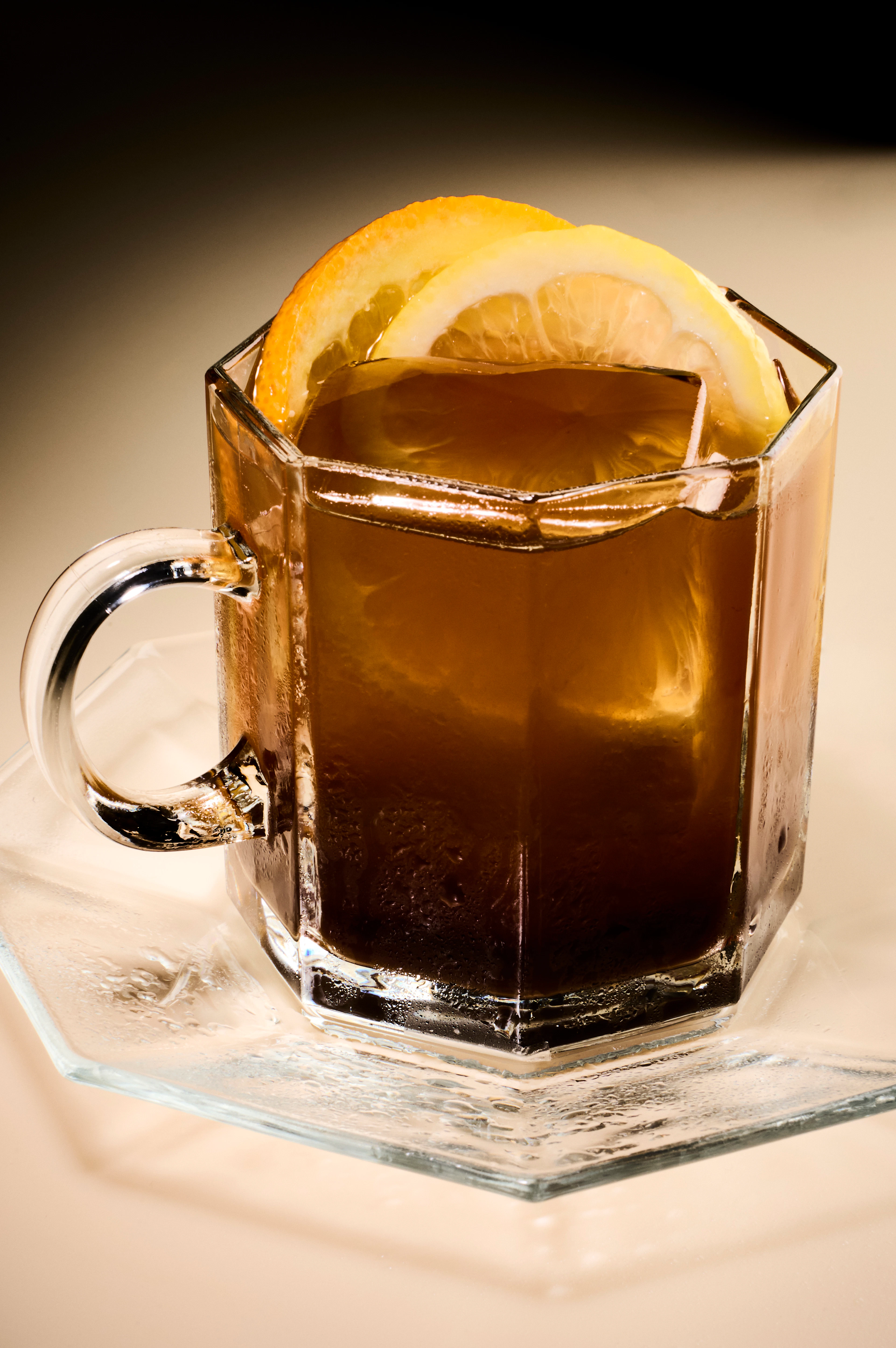 Siciliano cocktail with an orange garnish in a clear hexagonal glass mug