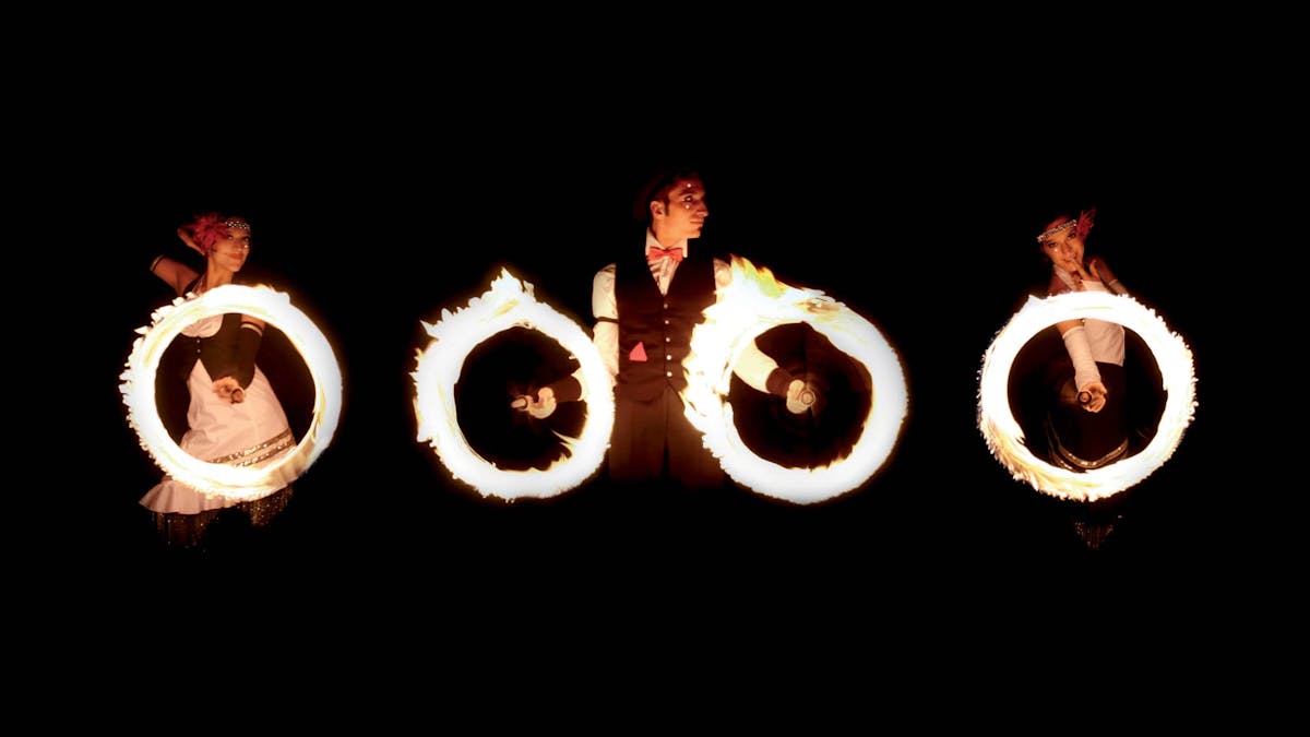 Feuershow mit drei Artisten, die in einer Reihe stehen und vier Feuerringe schwingen.