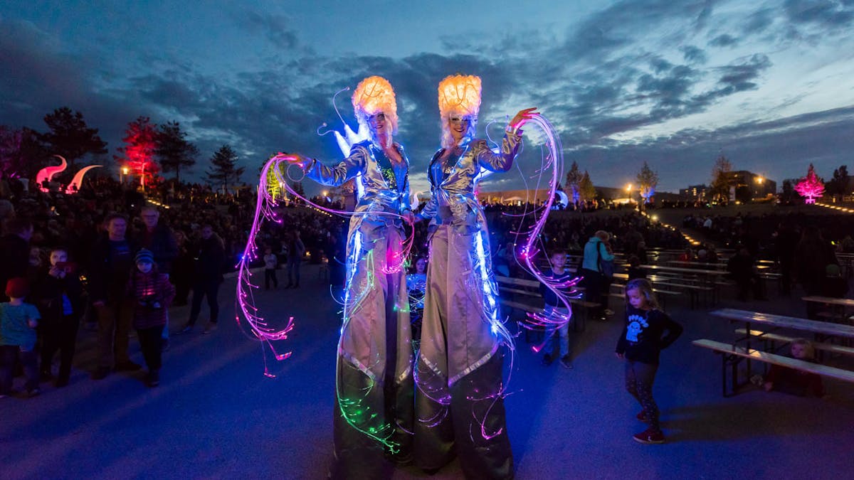 LED stilt walking-act in glowing silver costumes at a public event.