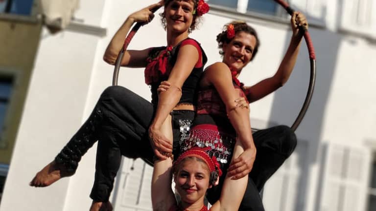 Strassenshow mit drei Gauklerinnen, die mit den Fingern in die Luft zeigen. 