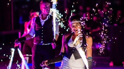 Zwei Performer in 20er Jahre Outfit machen Funkeneffekte in einer Feuershow. 
