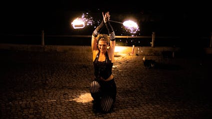 Performer kneels down and is swinging firepoi above her head. 