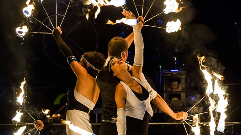 Feuershow mit drei Artisten, die in einer Reihe stehen und vier Feuerringe schwingen. 