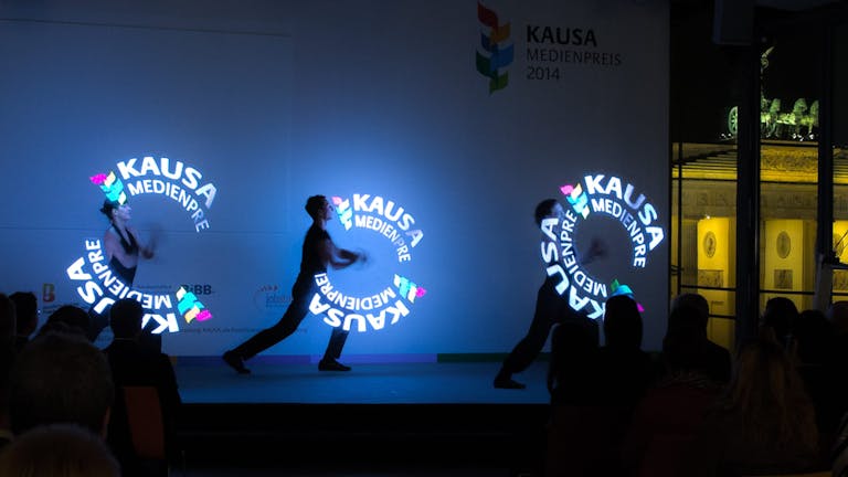 Lichtshow auf einer Bühne mit Artisten, die Pixelpoi mit Kausa Logo schwingen.
