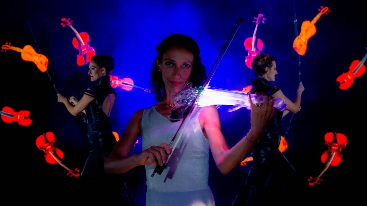 Violinist with Live-Violine and in the background Poi-Performer with glowing Violines. 